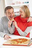 Senior Couple Sharing Takeaway Pizza In Kitchen