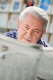 Elderly man with mustache reading paper in library