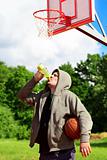 Man holding basketball and drink from bottle of water