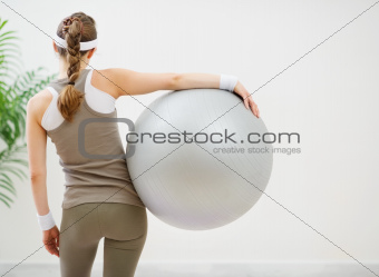 Athletic woman with fitness ball standing back to camera