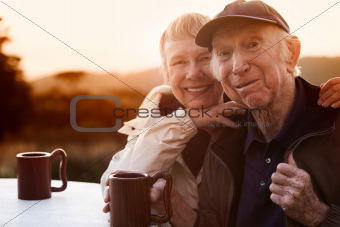 Cute senior couple in jackets outside at table smiling