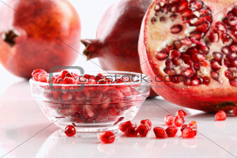 Ripe pomegranates and glass bowl of seeds on white