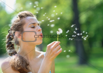 Young woman blowing away dandelion