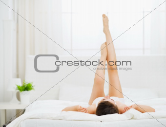 Woman in bed enjoying her beautiful legs. Rear view