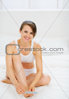 Happy woman sitting on bed and making manicure