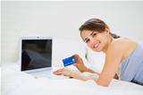 Smiling woman laying on bed with laptop and shopping on net
