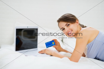Smiling woman laying on bed with laptop and shopping on net