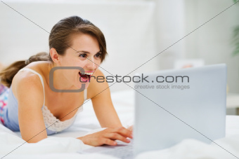 Woman laying on bed and suprisely looking in laptop