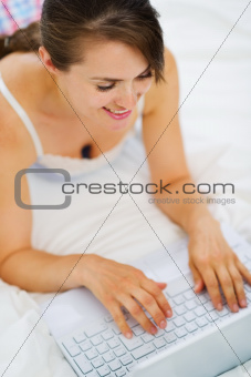 Woman laying on bed and working on laptop. Upper view