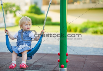 Baby swinging on swing on playground. Side view