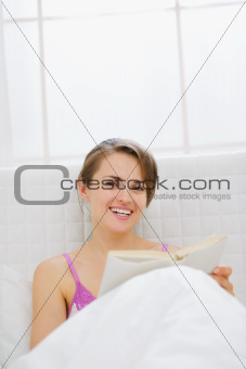 Happy woman in bed reading book