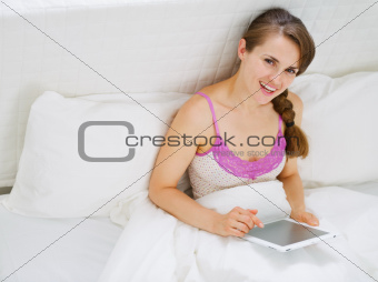 Happy woman sitting in bed and working on tablet pc