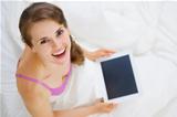 Smiling woman sitting in bed and using tablet pc. Upper view