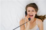Portrait of woman laying on bed and speaking phone. Upper view