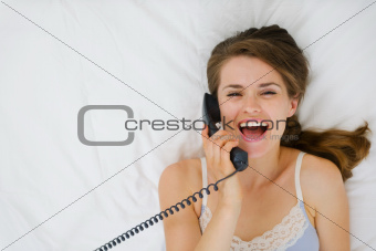 Portrait of woman laying on bed and speaking phone. Upper view