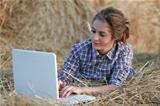 Country girl in lumberjack shirt with opened white laptop at haystack