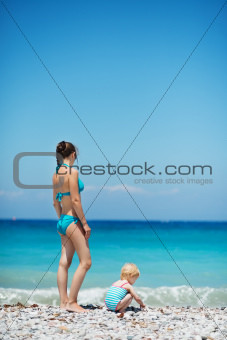 Mother and baby on sea shore. Rear view