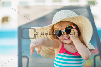 Portrait of baby in hat and glasses pointing in corner