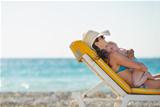 Mother with baby laying on sunbed on beach