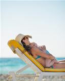 Mother hugging baby while laying on sunbed on beach