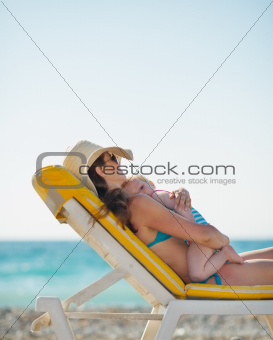 Mother hugging baby while laying on sunbed on beach
