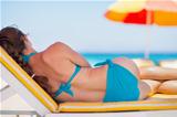 Woman laying on sunbed on beach. Rear view