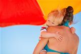 Baby embracing mother on beach under umbrella