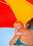 Mother holding baby looking on copy space on beach under umbrella