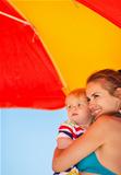 Mother and baby looking on copy space on beach under umbrella