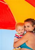 Portrait of mother and baby on beach under umbrella