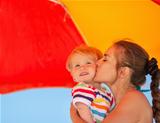 Mother kissing baby on beach under umbrella