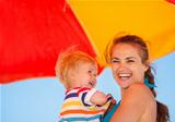 Portrait of happy mother and baby on beach under umbrella