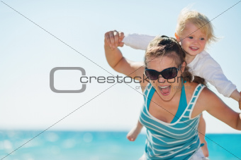 Baby piggybacking mother on beach