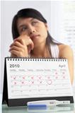 Sad woman with negative pregnancy test and calendar