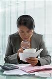 Asian businesswoman checking bills using magnifying glass