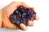Purple amethyst crystal in hand against white background