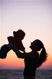 Silhouette of mother playing with baby in sunset