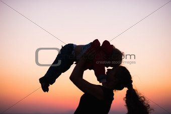 Silhouette of mother playing with baby in dusk