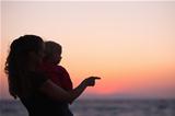 Silhouette of mother with baby in sunset pointing on copy space