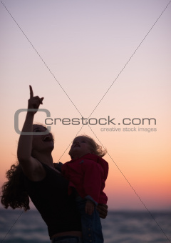 Silhouette of mother with baby in dusk pointing up on copy space