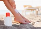 Bottle of sun block and female applying creme on leg on beach