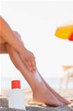 Bottle of sun block and female applying creme on leg on beach