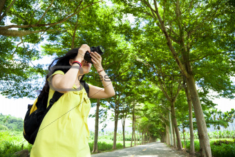 Young woman with backpack standing in the green forest taking photo