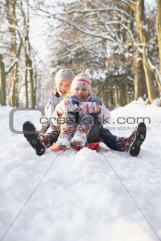 Boy And Girl Sledging Through Snowy Woodland
