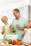 Grandchildren Helping Grandfather To Prepare Salad In Modern Kitchen
