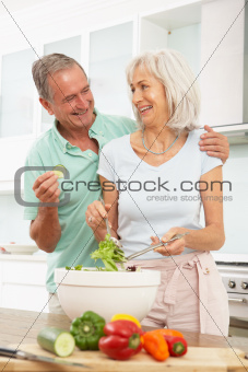 Senior Couple Preparing Salad In Modern Kitchen