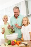 Grandchildren Helping Grandfather To Prepare Salad In Modern Kitchen