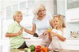 Grandchildren Helping Grandmother To Prepare Salad In Modern Kitchen