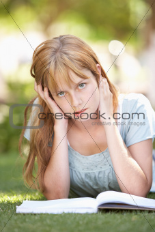Female Teenage Student Studying In Park Looking Puzzled