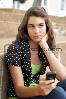 Unhappy Female Teenage Student Sitting Outside On College Steps Using Mobile Phone